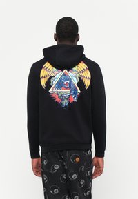 Zwarte hoodie met een kleurrijke graphic op de achterkant met een beer, vleugels en geometrische vormen. Zacht materiaal, capuchon met trekkoord, geribbelde manchetten.