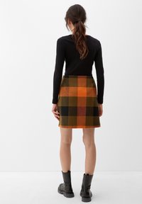 Minirok van een wolmix in een ruitpatroon van oranje, groen en zwart; heeft een hoge taille en rechte pasvorm, gecombineerd met zwarte laarzen.