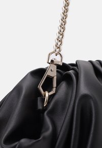 Sort håndtaske lavet af struktureret kunstlæder med en fletning af kædestrop og en detalje med guldfarvet lås for sikker lukning.
