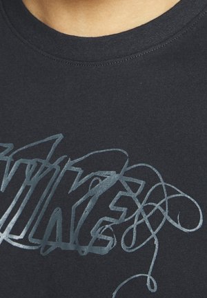 Zbliżenie na czarną koszulkę Nike z błyszczącym, srebrnym stylizowanym logo Nike na klatce piersiowej.