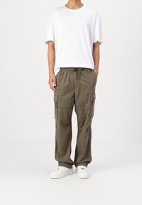 Olivgröna cargo-byxor med elastiskt midjeband och snörning, med sidofickor och avslappnad passform, tillsammans med en vit t-shirt.