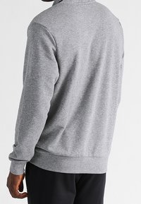 Šedá mikina s vysokým límcem, žebrovanými manžetami a lemem. Měkká látka s hladkou texturou, bez viditelných vzorů nebo ozdob.