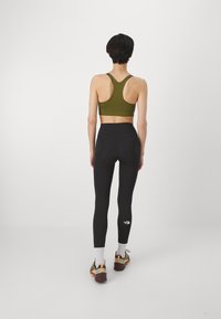Atletisk ensemble bestående av en olivgrön sport-bh och högmidjade svarta leggings, med en logodetalj på benet och textil med struktur.