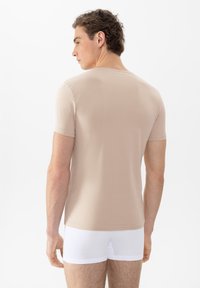 Beige t-shirt met korte mouwen en een ronde hals, gemaakt van zachte stof, met een getailleerde pasvorm, weergegeven vanuit de achterkant, gecombineerd met witte boxershorts.