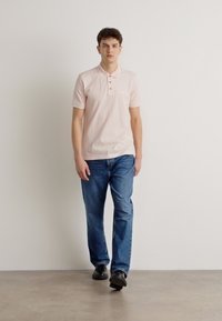 Ανοιχτό ροζ πόλο μπλούζα με κοντό μανίκι και πλάκα με δύο κουμπιά, συνδυασμένη με μπλε τζιν και μαύρα παπούτσια. Απλός και casual σχεδιασμός.