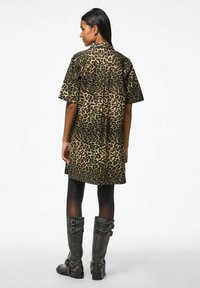 Abito a maniche corte con stampa leopardata in beige e nero, vestibilità ampia, lunghezza al ginocchio, con chiusura a bottoni sulla schiena, indossato con stivali grigi alti con fibbia.