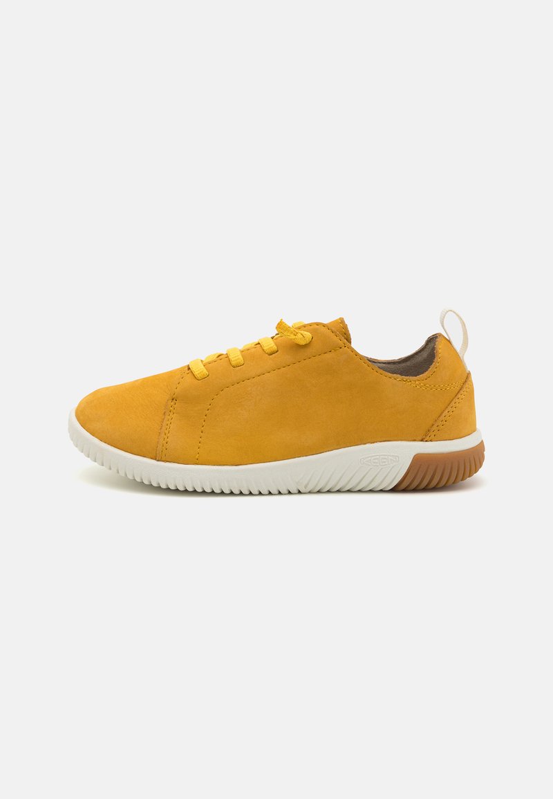 Żółte zamszowe sneakersy z białą gumową podeszwą, z płaskimi sznurowadłami, okrągłym noskiem i brązowym akcentem na pięcie.
