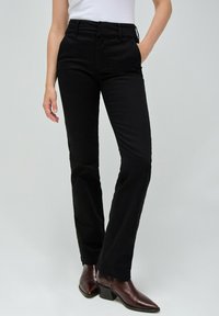 Pantaloni neri su misura con una vestibilità slim, dotati di vita alta, tasche laterali e una trama di tessuto liscia. Indossati con stivali con tacco marroni.