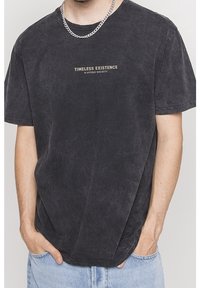 Czarny T-shirt z krótkim rękawem, wykonany z miękkiego materiału; posiada centralnie umieszczony napis "TIMELESS EXISTENCE" w jasnym kolorze, okrągły dekolt, luźny krój.