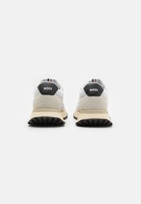Sneakers sportivi con una tomaia in rete bianca e suede grigio chiaro, dettagli neri sul tallone e una suola intermedia beige. Presentano un dettaglio a righe sul tallone.