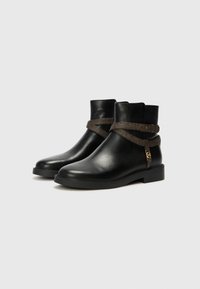 Black leather ankle boots with a textured brown strap around the upper, featuring a gold-tone zipper detail on the side and a flat sole.