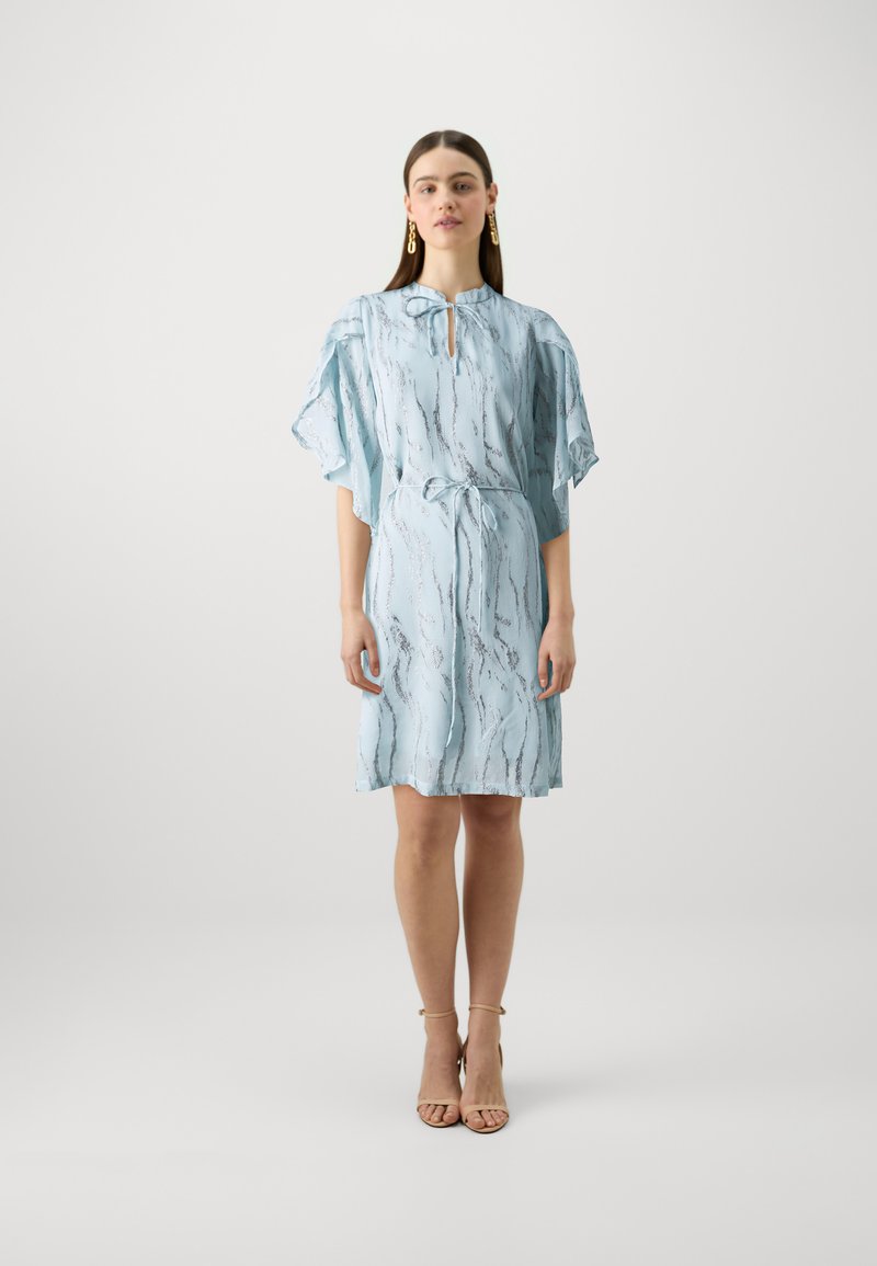 Robe courte bleu clair avec un décolleté en trou de serrure, des manches flottantes et une ceinture à nouer, ornée d'un motif argenté ondulé. Texture de tissu lisse.