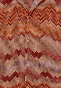 Vue de face d'un cardigan tricoté boutonné avec des motifs en zigzag dans des nuances de rouge, orange et beige.