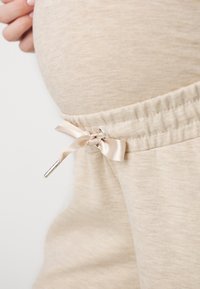 Beige mammabyxor med elastisk midjeband, med en satinband knytning och detaljer i silverfärg, tillverkade av ett mjukt, texturerat tyg.
