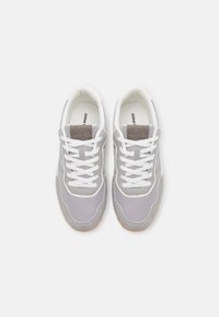 Pár šedých a bílých šněrovacích tenisek s světle hnědými podrážkami, zobrazených shora na čistém bílém pozadí.