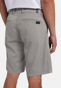 Pantaloni corti in cotone grigio chiaro con frontale piatto, tasche laterali e posteriori, e orlo cucito. Un piccolo etichetta di marca sulla tasca posteriore.
