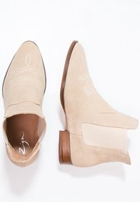 Botines de ante beige con puntera afilada, paneles laterales elásticos y costuras decorativas en la parte superior, con un tacón de madera.