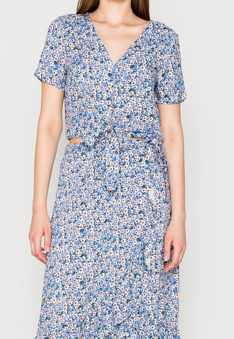 Haut court à fleurs bleu avec manches courtes et détail noué à l'avant, associé à une jupe assortie présentant un motif floral similaire et des volants.