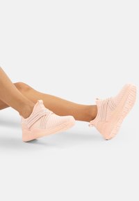 Helle rosa Sportschuhe aus strukturiertem Mesh, mit flexiblem Design, Zuglasche und einer dicken, gerillten Sohle für Unterstützung.