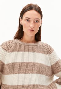 Pull rayé crème et marron avec une texture côtelée, un col rond et des épaules tombantes, présentant de larges rayures horizontales.