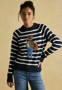 Tumesinise ja valge triibuline sviiter, millel on tikitud rebane ülikonnas ja teksades. Riboositud varrukad ja äär, valmistatud kudumiskangast.