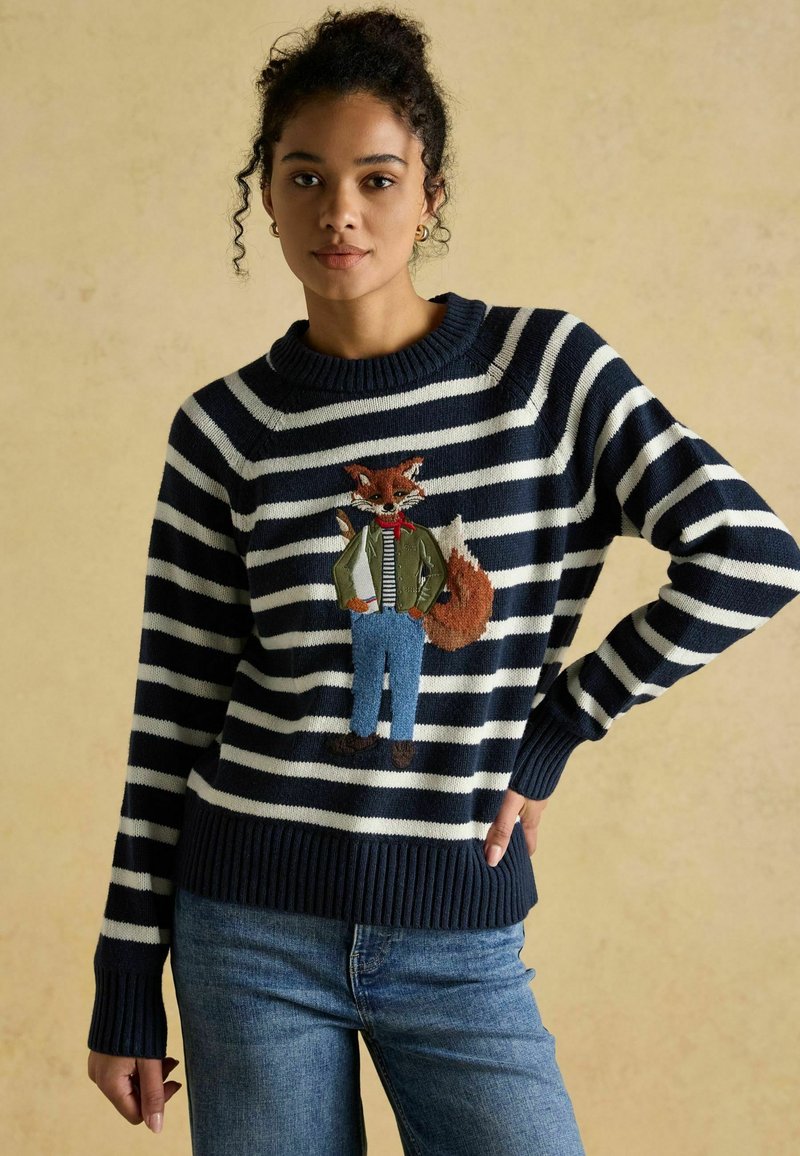 Tumesinise ja valge triibuline sviiter, millel on tikitud rebane ülikonnas ja teksades. Riboositud varrukad ja äär, valmistatud kudumiskangast.