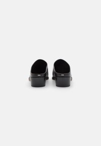 Mule in pelle nera con finitura liscia, design aperto arrotondato e tacco spesso a blocco. Presenta eleganti dettagli in hardware argentato.