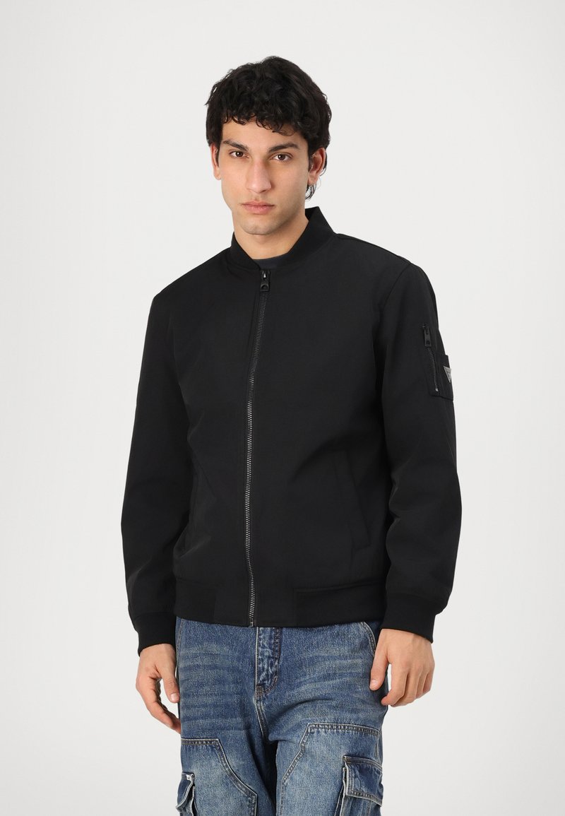 Black bomber jacket with a stand collar, front zipper, and side pockets. Features a zippered sleeve pocket, made of smooth fabric.
