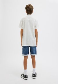 Camicia bianca a maniche corte con texture, pantaloni corti di denim blu con orli arrotolati, calze bianche e sneakers nere con dettagli bianchi.