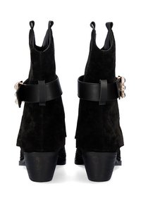 Botines negros de ante con una parte trasera curvada, detalles de correa de cuero y un tacón cuadrado, que presentan una textura suave y un diseño minimalista.