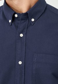 Laivastonsininen nappipaita, jossa klassinen kaulus, valkoiset napit ja rintatasku. Valmistettu teksturoidusta kankaasta.