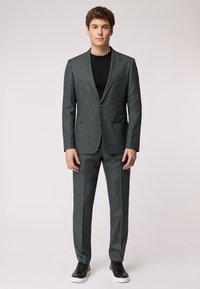 Completo a quadri grigio scuro con blazer a un bottone e pantaloni abbinati, accompagnato da una t-shirt nera e sneakers nere.