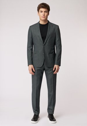 Dunkelgrauer karierten Anzug mit einreihigem Blazer und passender Hose, kombiniert mit einem schwarzen T-Shirt und schwarzen Sneakers.
