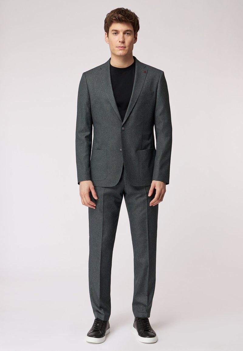 Completo a quadri grigio scuro con blazer a un bottone e pantaloni abbinati, accompagnato da una t-shirt nera e sneakers nere.