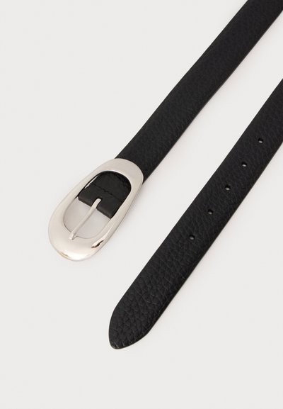 Ceinture en cuir noir texturé avec une boucle ovale argentée polie et plusieurs trous de réglage sur un fond clair.