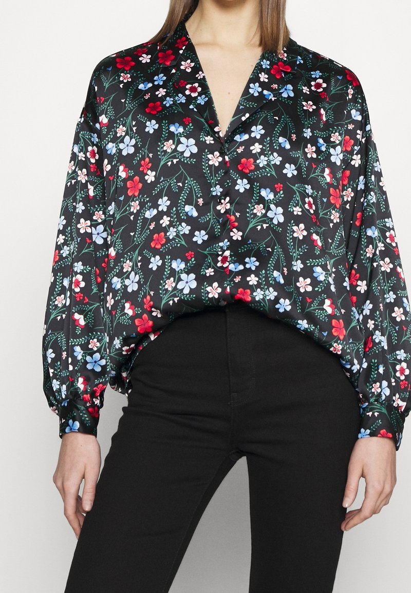Blusa nera a fiori con una combinazione di fiori rossi e blu, viti verdi, maniche lunghe, vestibilità rilassata e colletto.
