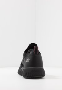 Scarpa da atletica nera con tomaia in maglia testurizzata e tallone in sintetico liscio, con un accento rosso sulla linguetta e un logo sul lato.