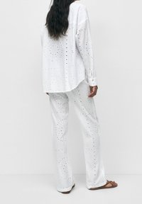 Ensemble deux pièces en coton blanc comprenant une chemise ample à cercles perforés et un pantalon large assorti avec une texture similaire.