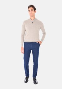 Maglione grigio chiaro con zip e jeans sartoriali blu scuro, completati da scarpe eleganti nere. Texture morbide e design aderente.
