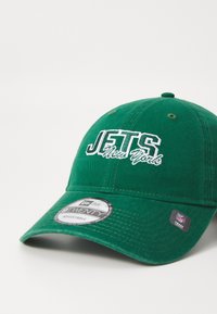Zelena bejzbol kapa s podesivim remenom, s vezom "JETS New York" u bijeloj boji. Ravni rub i teksturirana tkanina.