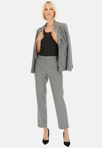 Szary marynarka o dopasowanym kroju i pasujące spodnie, materiał wydaje się gładki, strukturalny design, czarny dopasowany top pod spodem, noszone z wysokimi obcasami.
