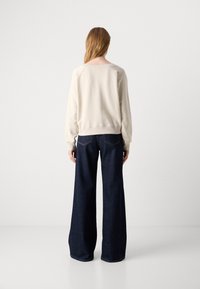 Felpa crema con maniche lunghe e polsini a costine, abbinata a jeans larghi blu scuro con tasche posteriori e cuciture visibili.