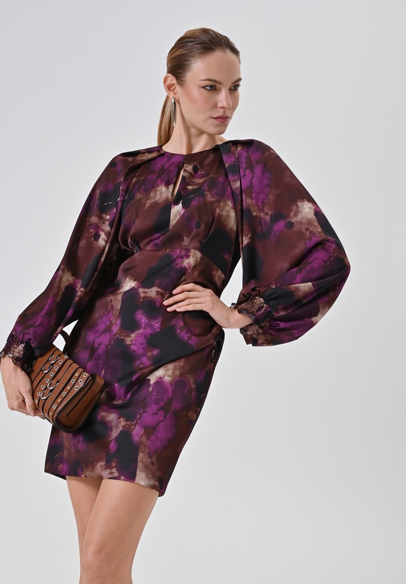 Lila-braun gemustertes Kleid mit Puffärmeln und einem Schlüsselloch-Ausschnitt, kombiniert mit einer braunen Umhängetasche mit silberner Hardware.