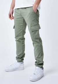 Lysgrønne cargo bukser med sidelommer, tætsiddende pasform og forstærkede syninger. Sammen med hvide sneakers. Sømløs design forbedrer funktionaliteten.
