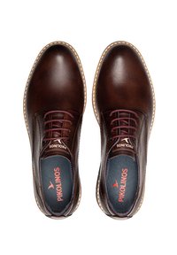 Zapatos de cuero marrón con un acabado suave, puntera redonda, costuras blancas en contraste y cordones de color burdeos. El interior presenta una plantilla azul con marca.