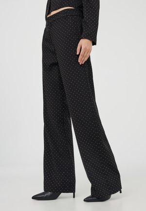 Pantaloni neri a gamba larga con pois bianchi abbinati a scarpe nere con tacco a punta e una blusa con pois abbinata.
