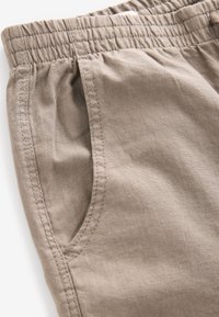I pantaloni corti in cotone stretch beige presentano una vita elastica, tasche laterali e una texture liscia con cuciture dettagliate lungo i bordi.