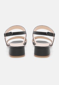 Zwarte leren sandaaltjes met hak, open achterkant, verstelbare enkelband en afgeronde blokhak. Glad interieur en minimalistisch ontwerp.