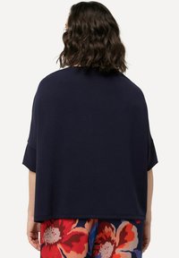 Maglione in maglia oversize blu navy con maniche corte, caratterizzato da una texture morbida e un design morbido, abbinato a pantaloni floreali colorati.