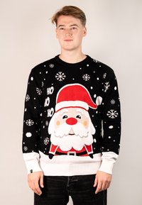 Schwarzer Strickpullover mit einem großen Santa-Gesicht, rotem Hut und weißem Bart. Weiße Schneeflocken und der Text "HO HO HO" sind auf einem schwarzen Hintergrund verteilt.